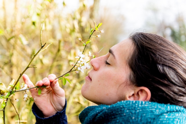 Woman in a coat smelling a brnch full of flowers. 